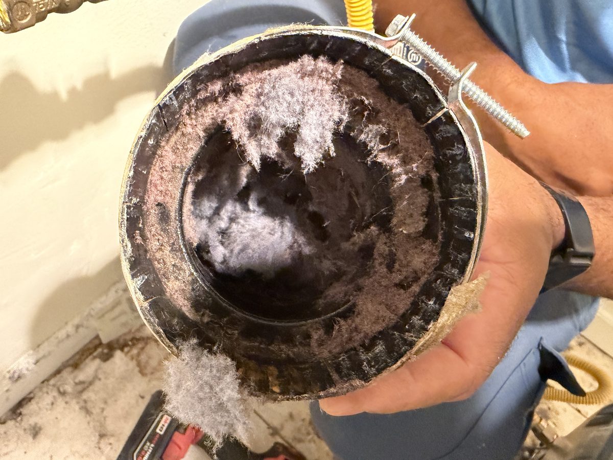 A length of dryer vent pipe held up to show the lint packed inside it