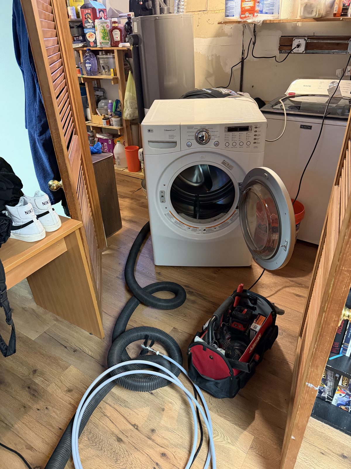 A laundry room set up for a dryer vent cleaning, hoses and a tool bag laid out on the floor