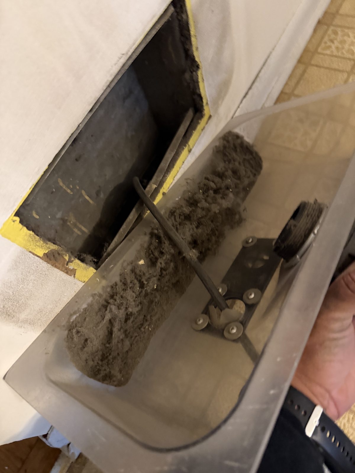 A clear catch tray held under a return opening, the brush inside it thick with the dust it pulled out
