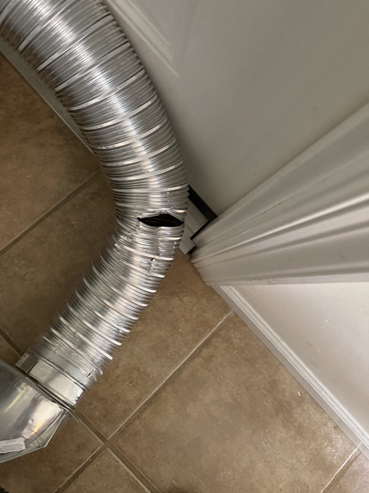 A foil transition duct with a split in its side, lying on a tile floor