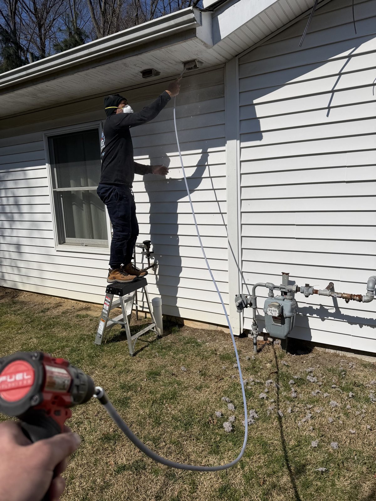 An AMG technician feeding a rotary cleaning line into a vent under the eaves