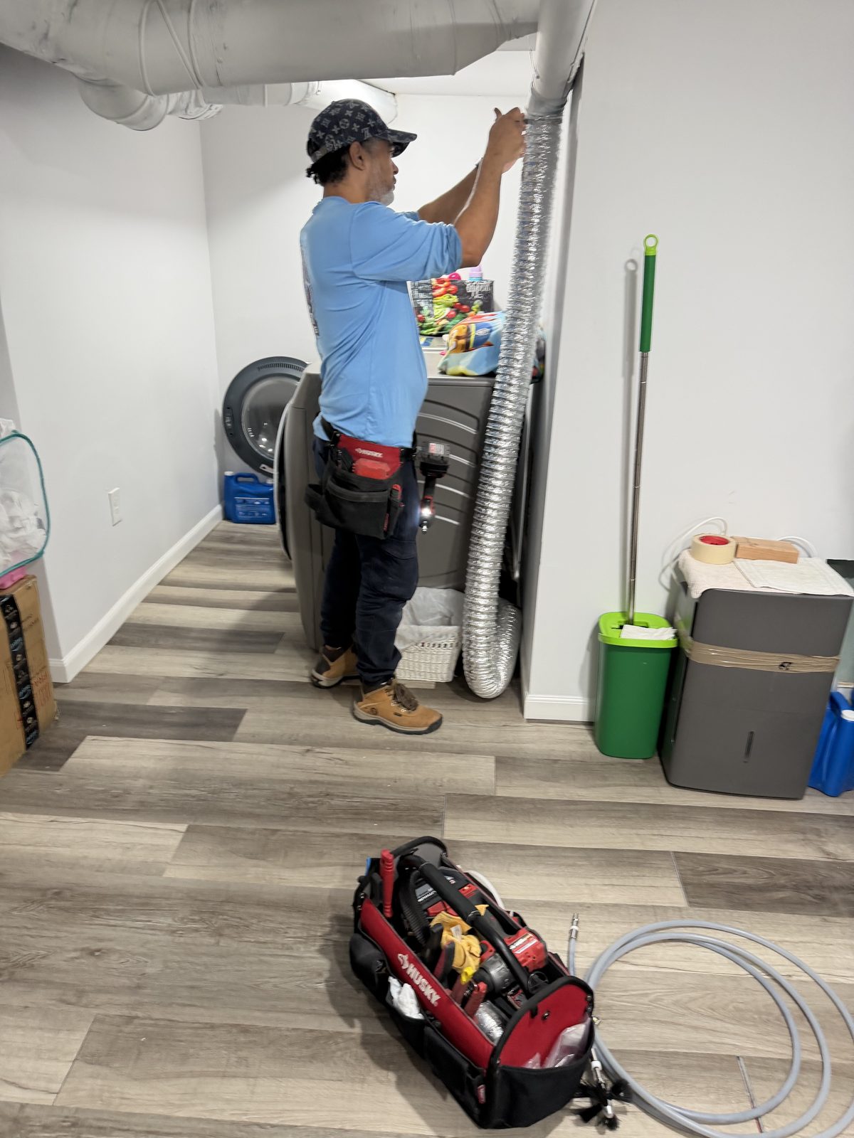 An AMG technician in a laundry room reaching up to the foil dryer duct