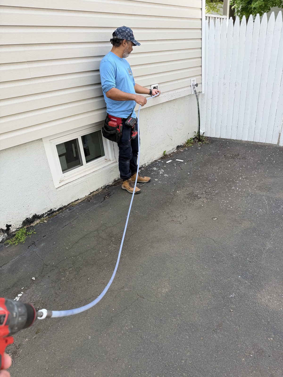 An AMG technician at an outside dryer vent, feeding the cleaning line into the run
