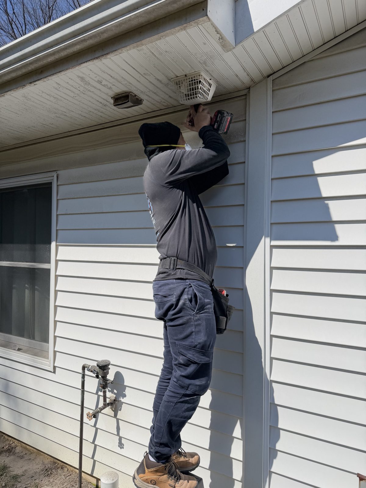 An AMG technician working a drill at a caged vent under the eaves