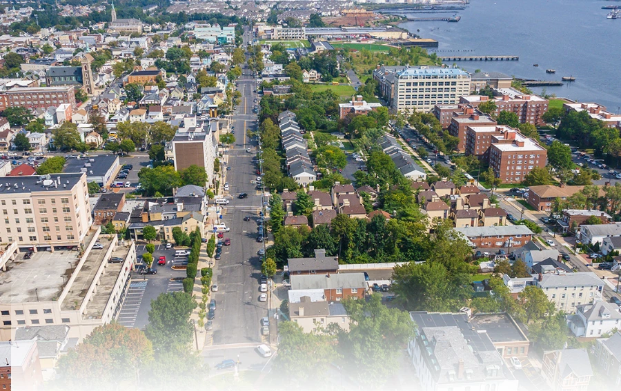 Aerial view of Middlesex County, NJ, showcasing a mix of residential and commercial buildings with tree-lined streets and a waterfront in the background.