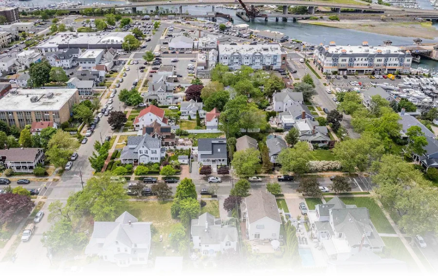 Aerial view of a suburban neighborhood in Monmouth County, NJ, with houses, trees, and a waterfront in the background.